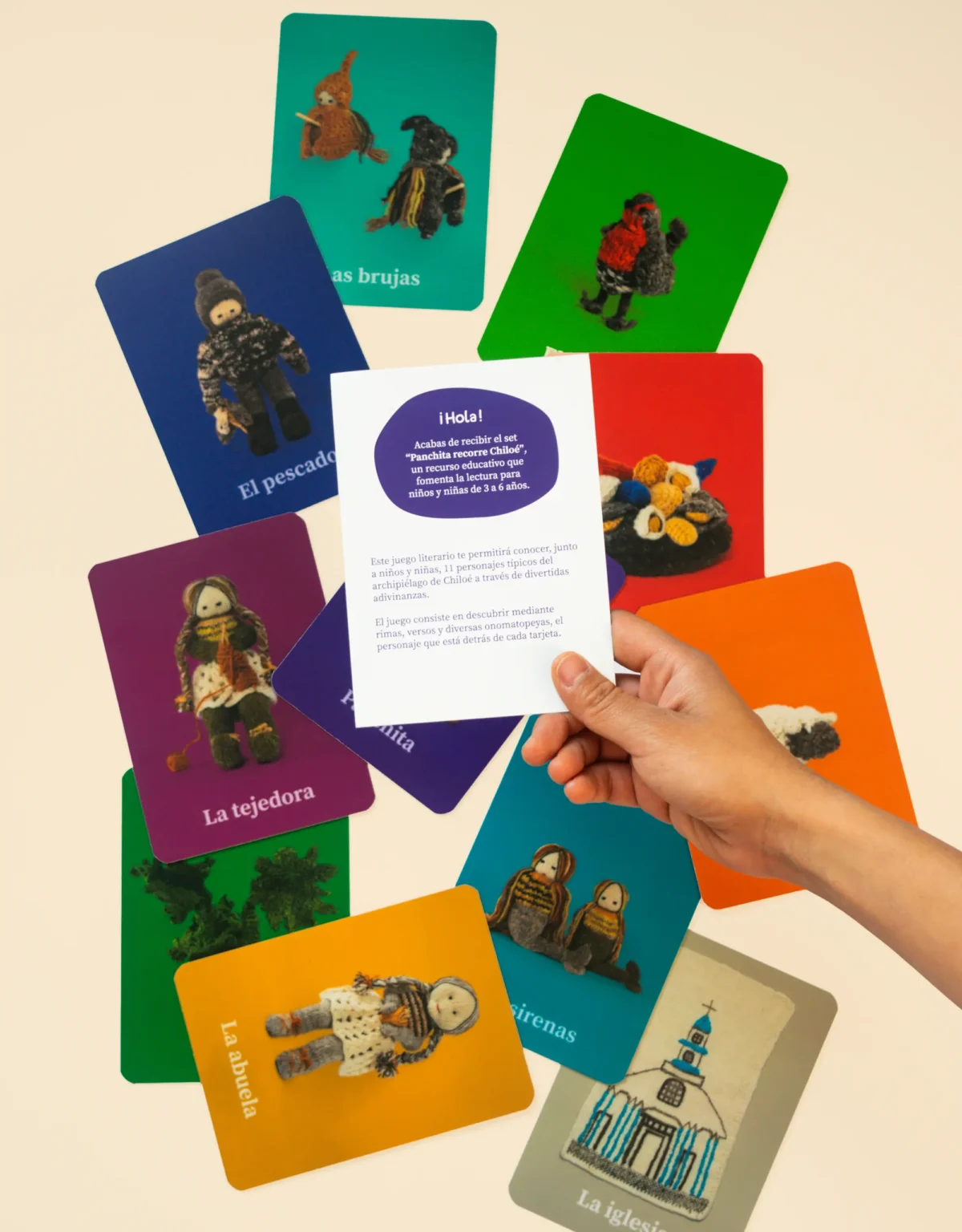 Una mano sostiene un folleto con texto informativo sobre el set Panchita recorre Chiloé, en el fondo se ven las tarjetas del set esparcidas en la superficie.