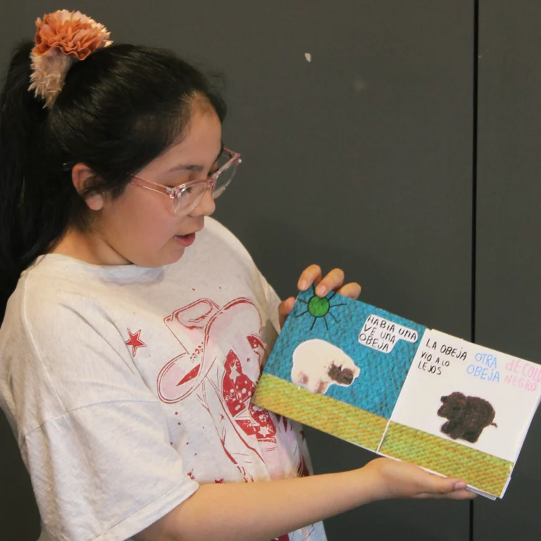 Niña sostiene un libro hecho por ella misma con imágenes de ovejas tejidas.