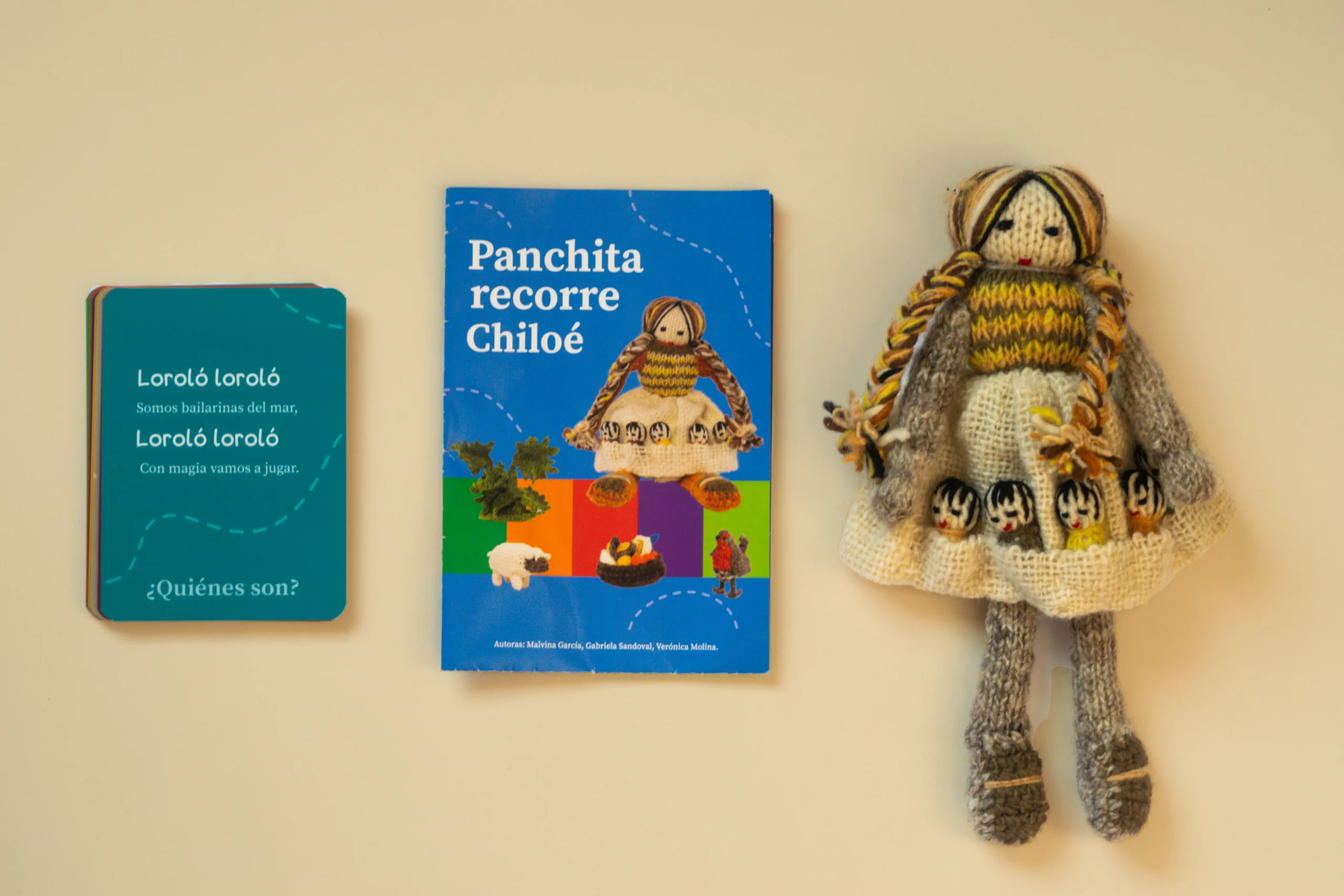 El Set Panchita recorre Chiloé combina tarjetas de colores, folleto y muñeca de lana Panchita con largas trenzas y un vestido beige que guarda a sus cinco hijos sobre una superficie lisa.