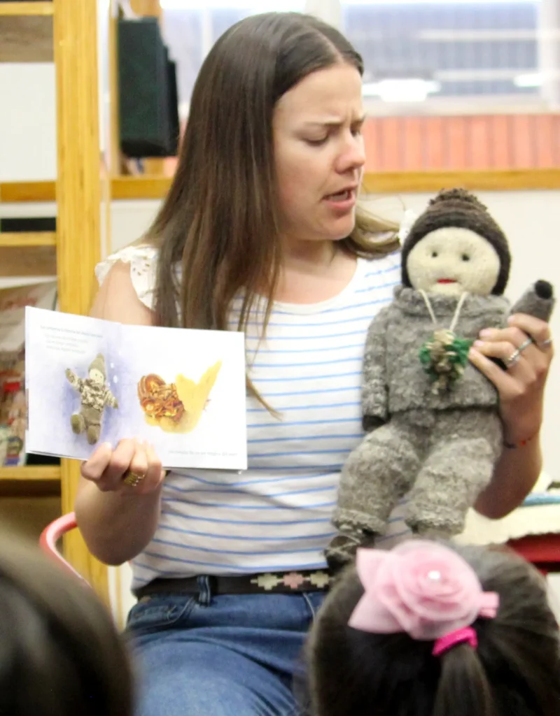 Mediadora sostiene un libro ilustrado desplegable y un muñeco tejido mostrándolo a un grupo de niños y niñas.
