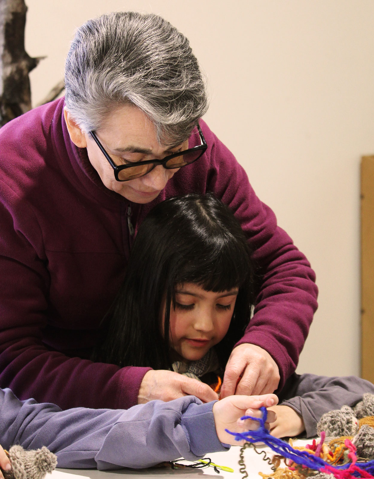 Artesana guía a una niña mientras trabajan juntas con lanas de colores sobre una mesa.