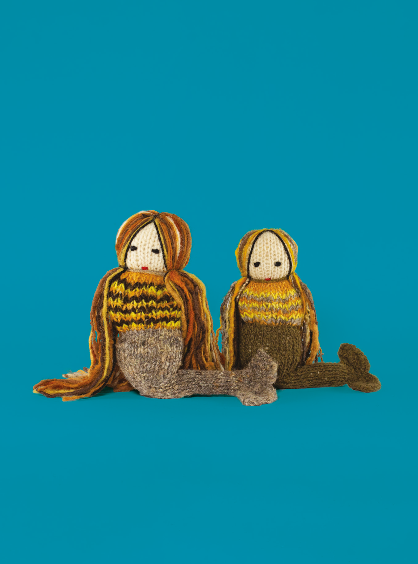 Muñecas de lana que representan sirenas sobre fondo azul.