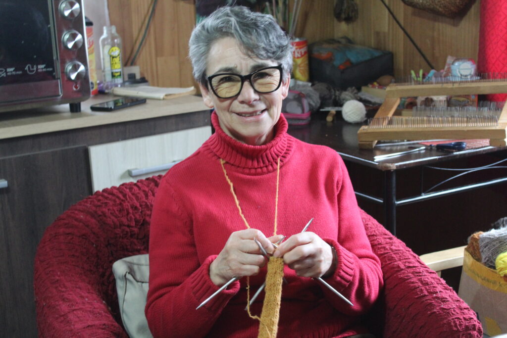 Malvina García, artesana dalcahuina, teje a palillos mientras sonríe.
